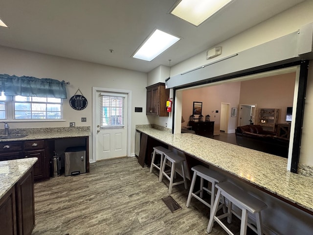 kitchen featuring light stone countertops, dark brown cabinetry, a kitchen breakfast bar, and dark wood-type flooring