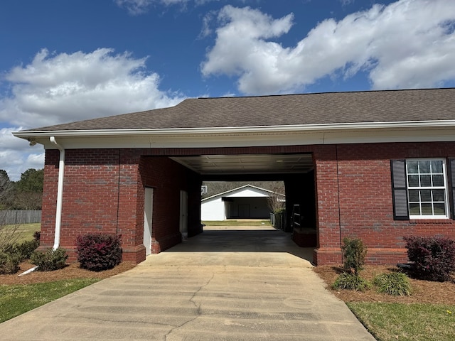 exterior space with roof with shingles, an attached carport, concrete driveway, and brick siding