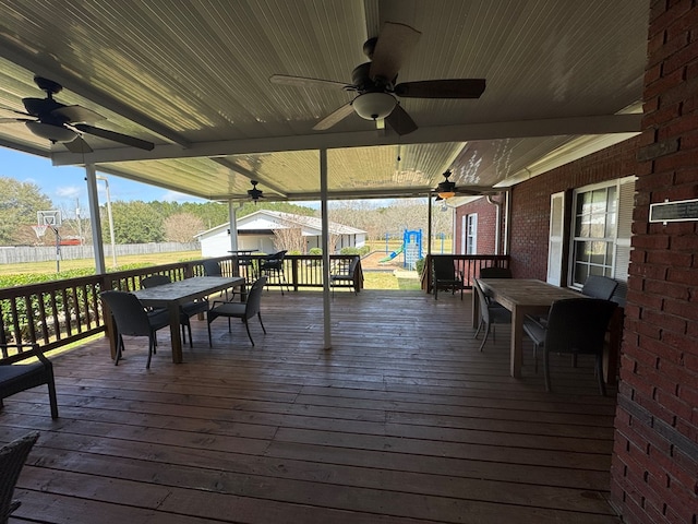 wooden deck featuring outdoor dining area, a playground, fence, and a ceiling fan