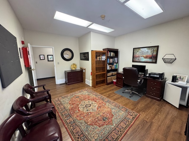 home office featuring a skylight, baseboards, and wood finished floors