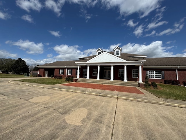 greek revival inspired property featuring a front yard, covered porch, and brick siding