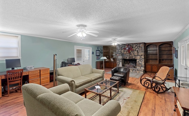 living room featuring a textured ceiling, ornamental molding, light hardwood / wood-style floors, and a stone fireplace