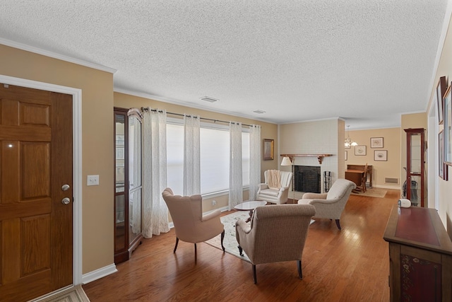 living room with wood-type flooring, a brick fireplace, a textured ceiling, and ornamental molding