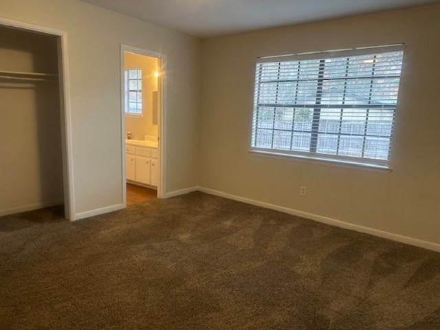 unfurnished bedroom featuring ensuite bathroom, dark carpet, and a closet