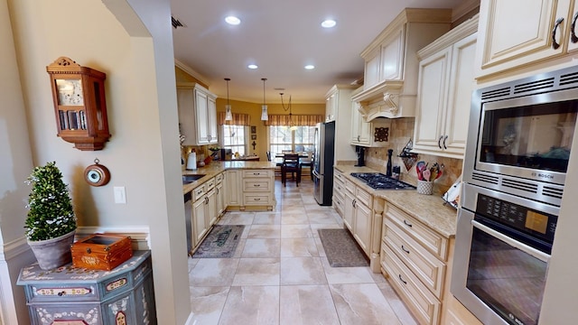 kitchen featuring appliances with stainless steel finishes, pendant lighting, tasteful backsplash, light stone counters, and cream cabinetry