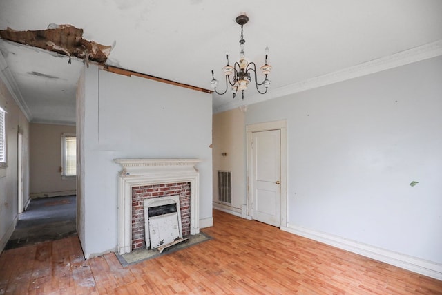 unfurnished living room with crown molding, a brick fireplace, a notable chandelier, and hardwood / wood-style floors