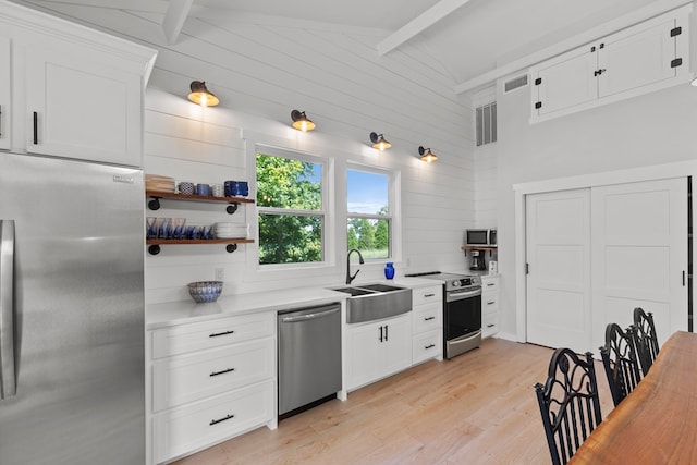 kitchen with sink, vaulted ceiling with beams, appliances with stainless steel finishes, white cabinets, and light wood-type flooring