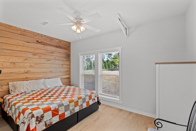 bedroom featuring light hardwood / wood-style floors, ceiling fan, and wooden walls