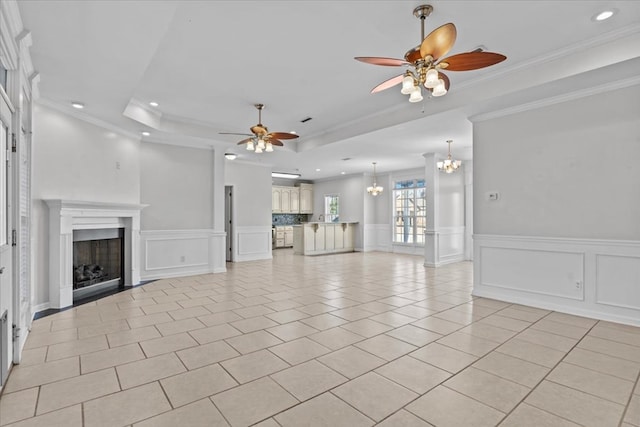 unfurnished living room with light tile patterned floors, ornamental molding, ceiling fan with notable chandelier, and a tray ceiling