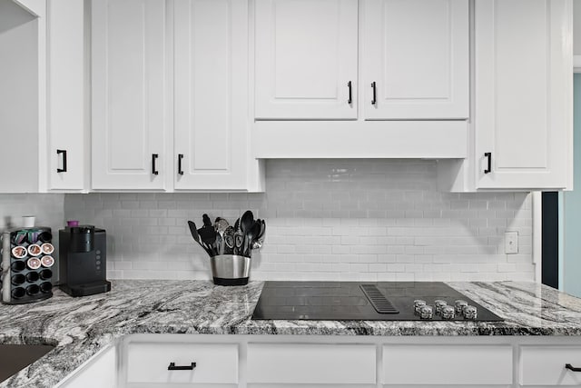 kitchen featuring white cabinets, black electric stovetop, light stone countertops, and tasteful backsplash