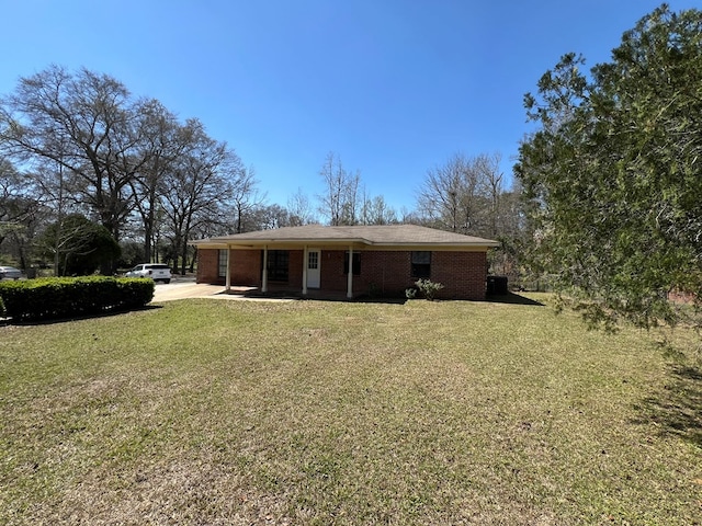 back of property with brick siding, a lawn, and a carport