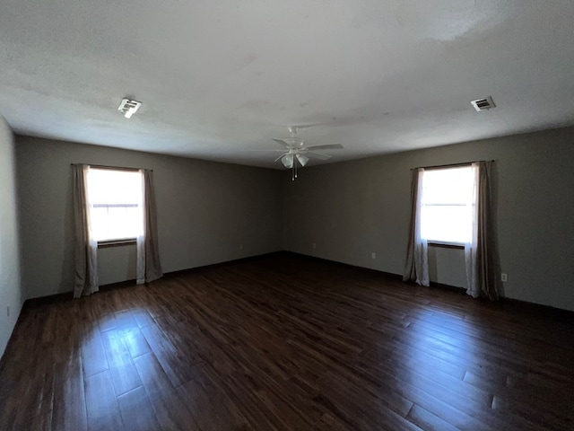 spare room featuring plenty of natural light, ceiling fan, and dark wood finished floors