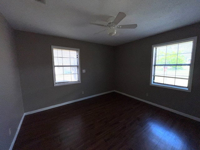 spare room with baseboards, plenty of natural light, dark wood-style floors, and a ceiling fan