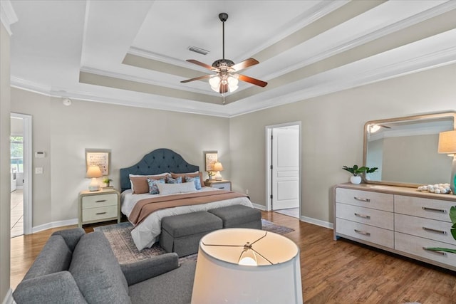 bedroom featuring visible vents, wood finished floors, a raised ceiling, and crown molding