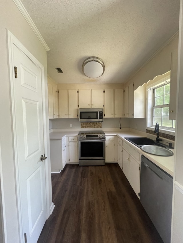 kitchen with appliances with stainless steel finishes, a sink, dark wood finished floors, a textured ceiling, and light countertops