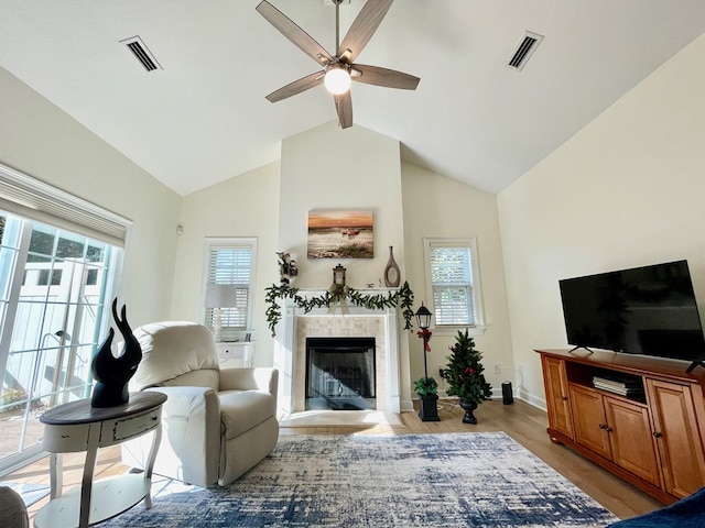 living room featuring vaulted ceiling with beams, light hardwood / wood-style floors, a healthy amount of sunlight, and a tiled fireplace