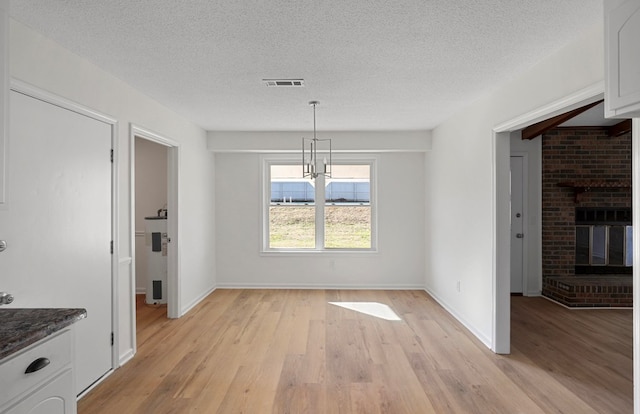 unfurnished dining area featuring a fireplace, light hardwood / wood-style floors, and a textured ceiling