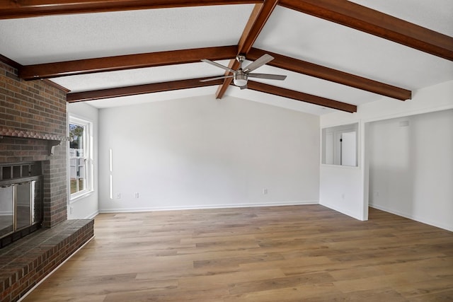 unfurnished living room with vaulted ceiling with beams, light hardwood / wood-style floors, a brick fireplace, and a textured ceiling