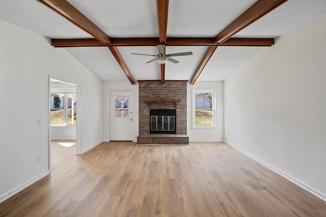 unfurnished living room featuring a fireplace, lofted ceiling with beams, a textured ceiling, and light wood-type flooring