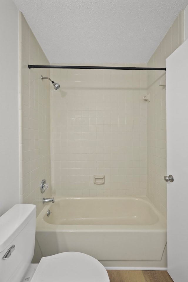 bathroom with hardwood / wood-style flooring, toilet, tiled shower / bath combo, and a textured ceiling