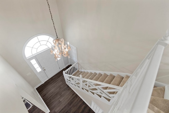 staircase with wood-type flooring, a towering ceiling, and an inviting chandelier