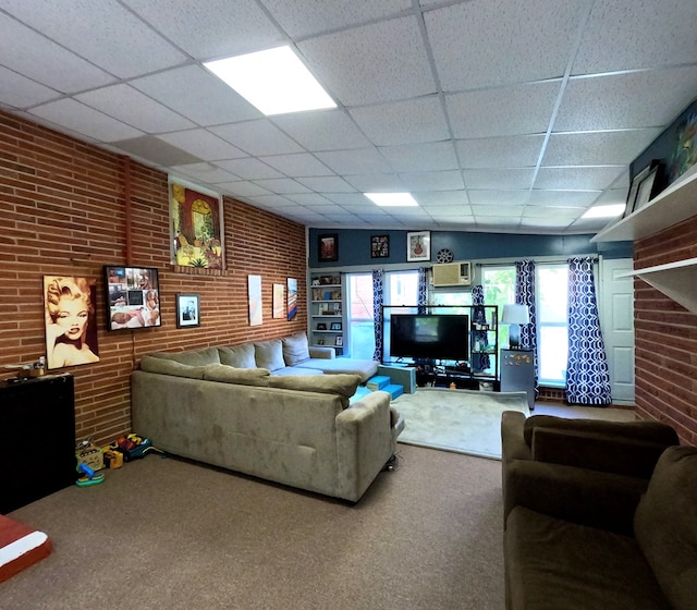 carpeted living room featuring a drop ceiling and brick wall