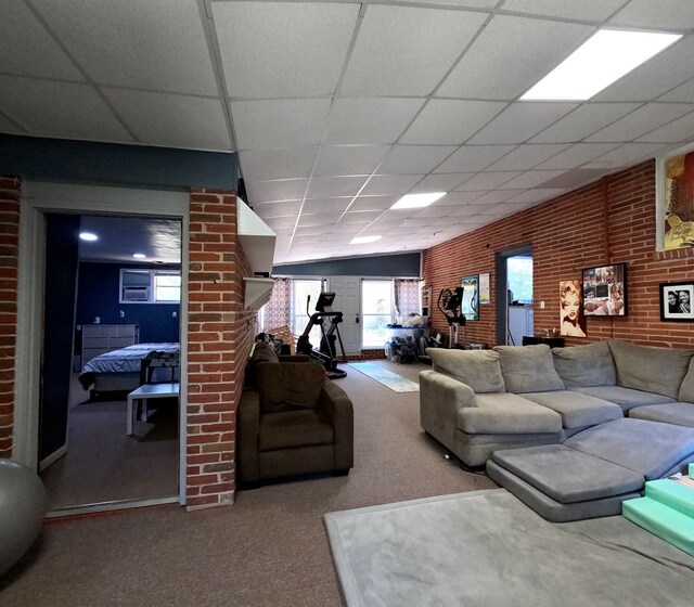 living room with carpet floors, a paneled ceiling, and brick wall