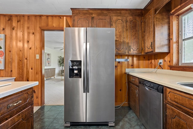 kitchen featuring dark tile patterned floors, stainless steel appliances, ceiling fan, and wooden walls