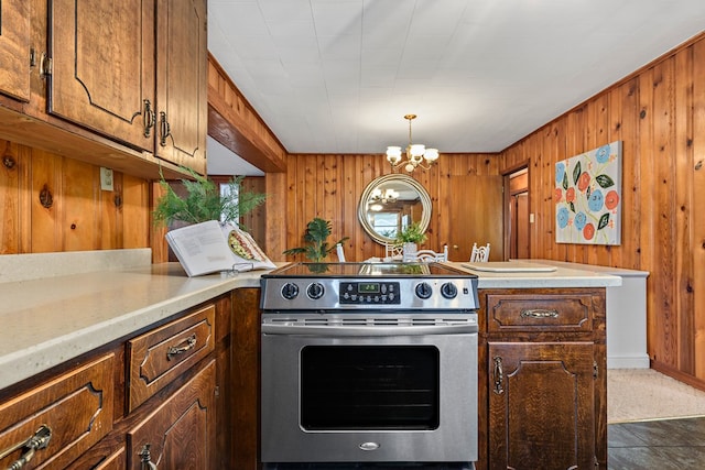 kitchen featuring dark tile patterned floors, stainless steel range with electric cooktop, wooden walls, and an inviting chandelier