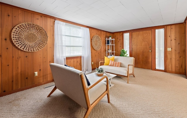 sitting room with ornamental molding, light colored carpet, and wooden walls