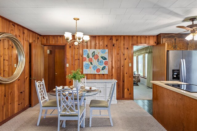 dining space with ceiling fan with notable chandelier, light carpet, and wooden walls