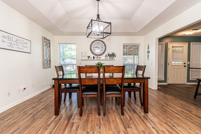 dining room featuring baseboards, wood finished floors, an inviting chandelier, and a raised ceiling