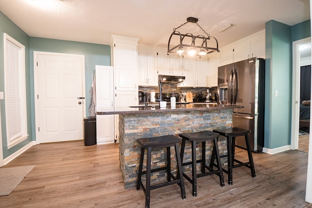kitchen featuring backsplash, light wood-style floors, white cabinets, stainless steel refrigerator with ice dispenser, and under cabinet range hood