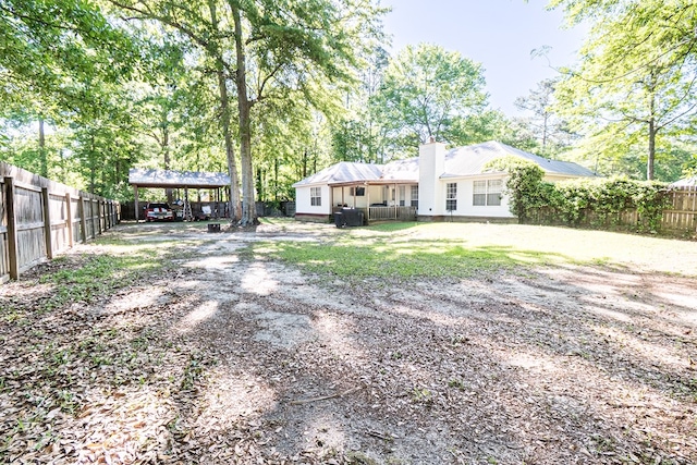 rear view of property with fence, dirt driveway, a chimney, and a carport