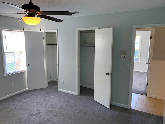 unfurnished bedroom featuring ceiling fan, carpet floors, a textured ceiling, and multiple closets