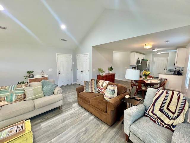 living area featuring visible vents, baseboards, high vaulted ceiling, and wood finished floors