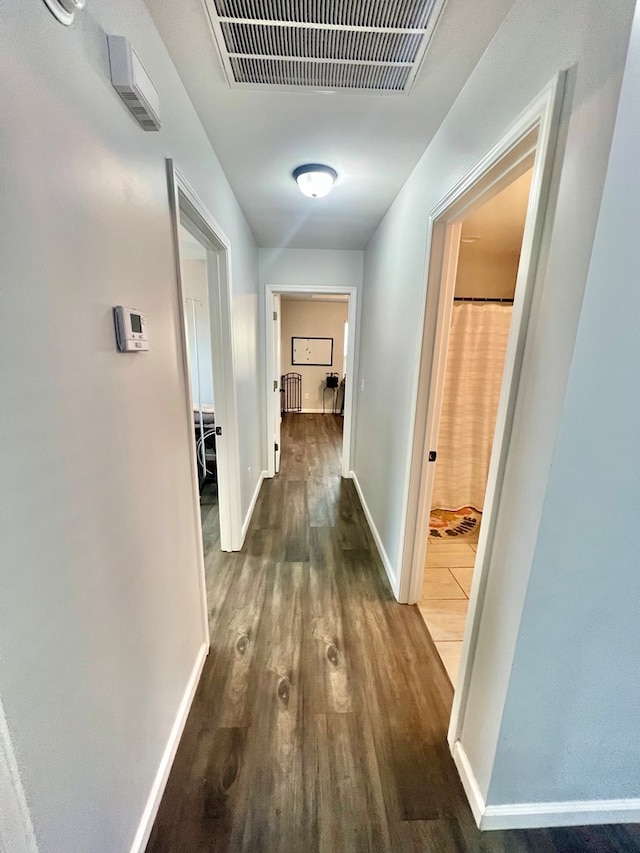 corridor featuring visible vents, dark wood-type flooring, and baseboards