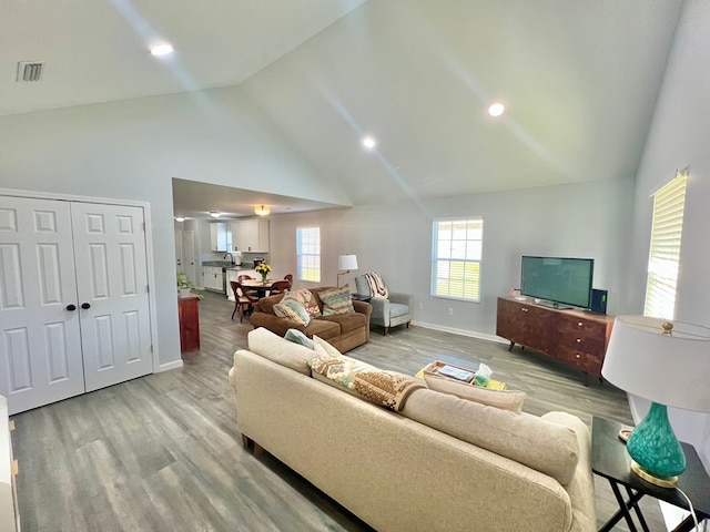 living room with visible vents, baseboards, light wood-style floors, and high vaulted ceiling