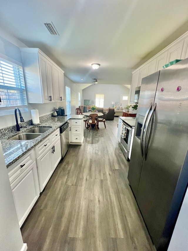 kitchen featuring visible vents, a peninsula, stainless steel appliances, white cabinetry, and a sink