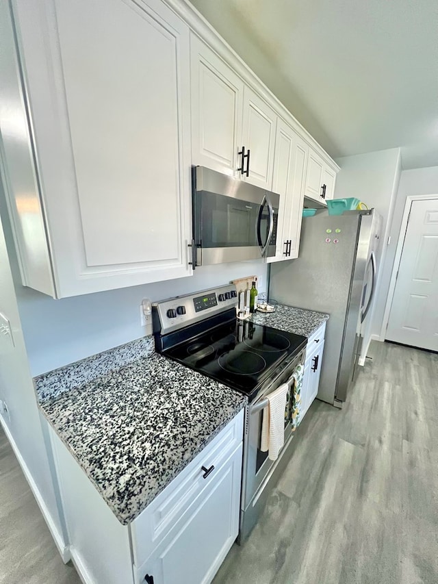 kitchen with light stone countertops, baseboards, light wood finished floors, appliances with stainless steel finishes, and white cabinetry