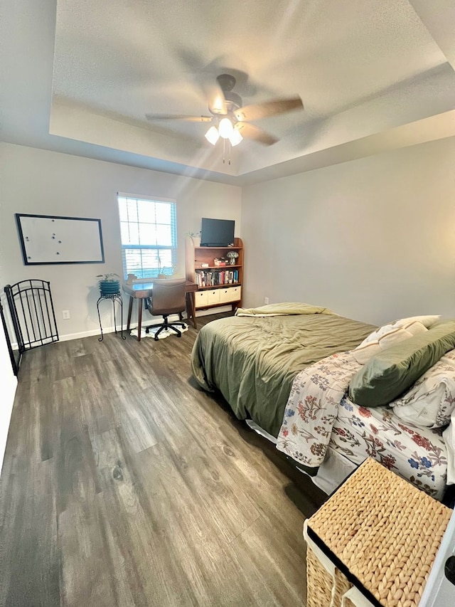 bedroom with a ceiling fan, wood finished floors, baseboards, a textured ceiling, and a raised ceiling