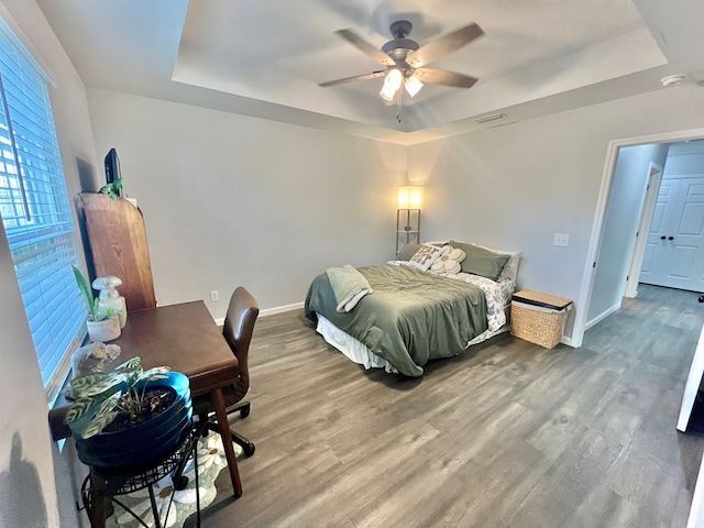 bedroom featuring a raised ceiling, wood finished floors, and baseboards