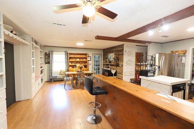 bar featuring stainless steel refrigerator, ceiling fan, beamed ceiling, and light wood-type flooring