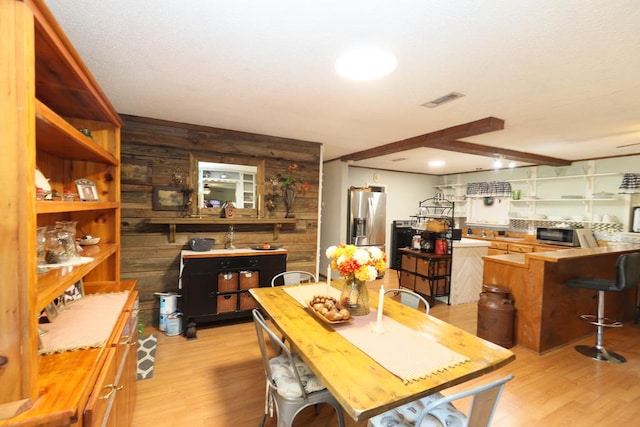 dining space with beamed ceiling, light wood-type flooring, and wooden walls