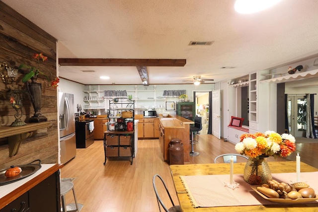 dining room with beamed ceiling, ceiling fan, light wood-type flooring, and a textured ceiling