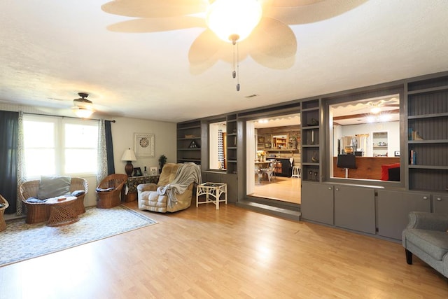 living room featuring built in shelves, ceiling fan, and light hardwood / wood-style flooring