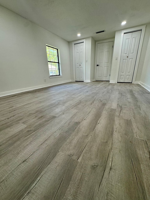 unfurnished bedroom featuring baseboards, recessed lighting, multiple closets, and wood finished floors