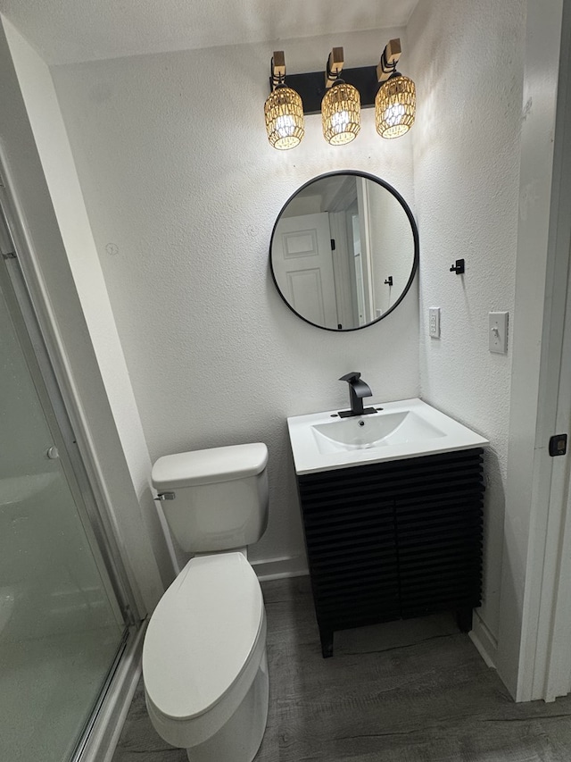 bathroom with a stall shower, wood finished floors, vanity, baseboards, and toilet