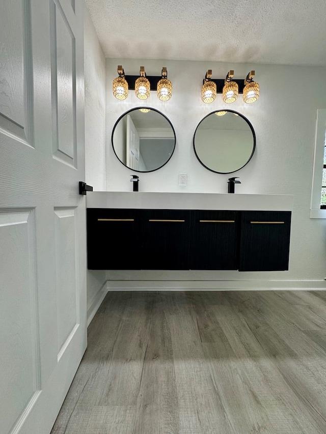 bathroom with baseboards, double vanity, a textured ceiling, and wood finished floors