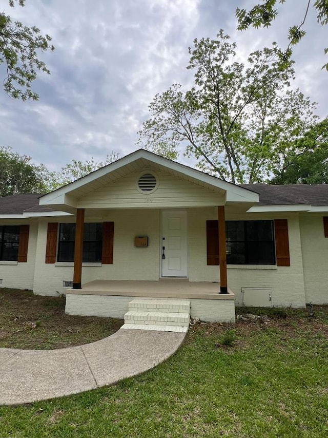 ranch-style house featuring brick siding, roof with shingles, and covered porch
